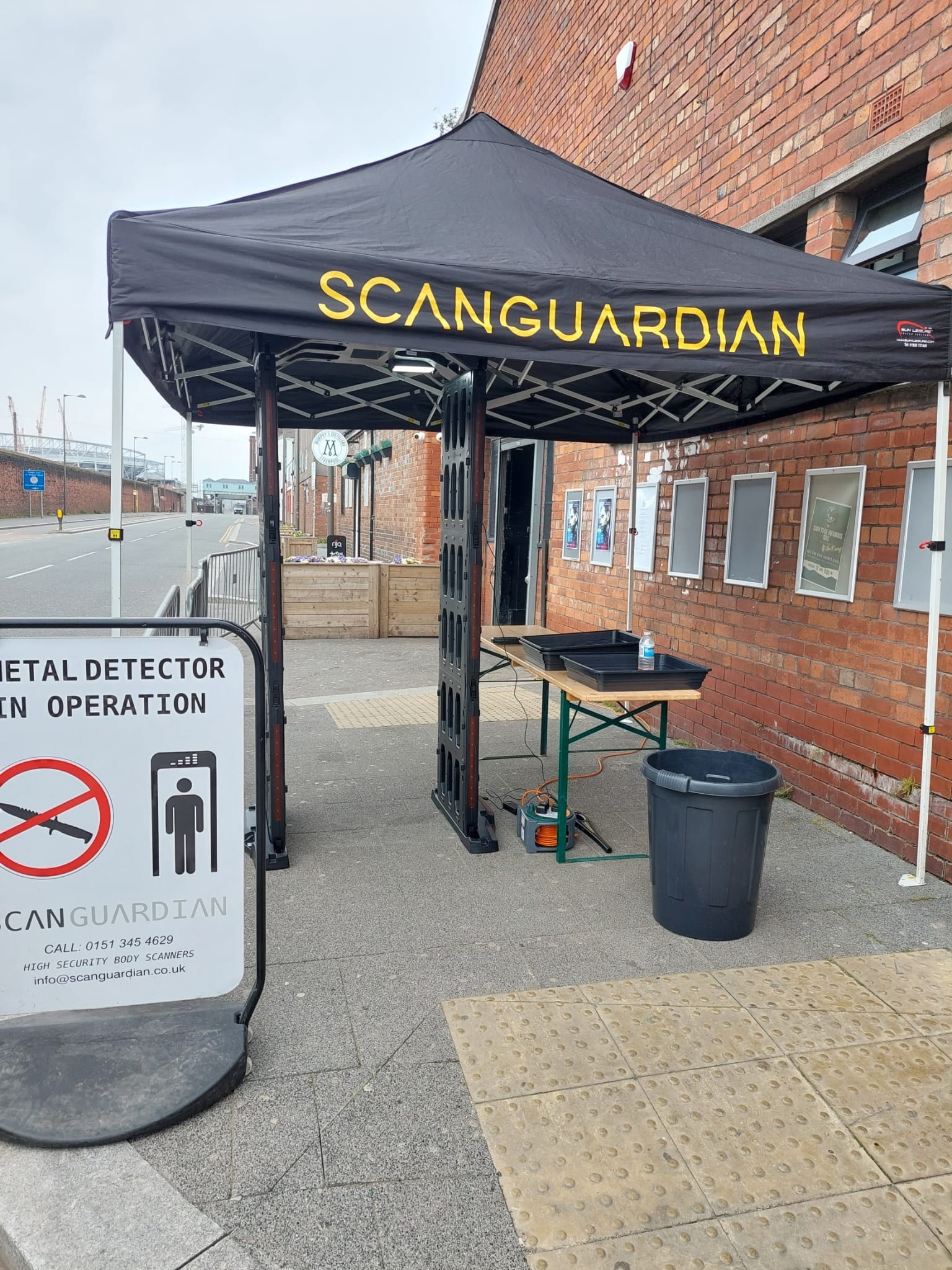 ScanGuardian branded tent and arch scanner outside a brick venue with metal detector in operation sign